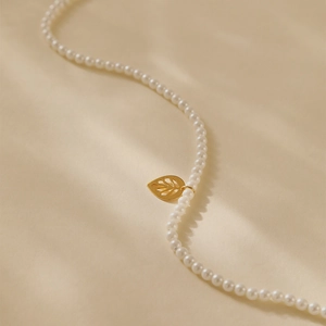 Detail van elegante parelketting met gouden blad hanger op warme getextureerde achtergrond