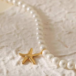 Gedetailleerde close-up van handgemaakte parelketting met een gouden zeester hanger