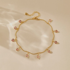 Détail d'un bracelet de cheville doré avec dix pierres roses en forme de cœur et reflets