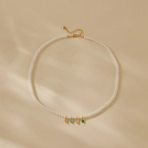 Detail van parelketting met vier gekleurde hartvormige hangers en verstelbare gouden sluiting