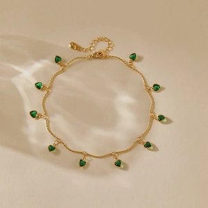Gros plan d'une chaîne de cheville dorée avec dix pendentifs en cœur de zircon vert