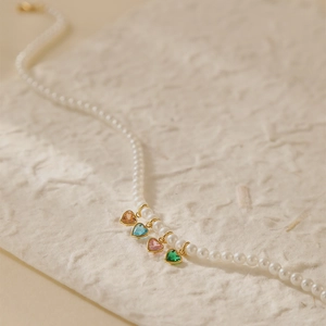 Detail van parelketting met kleurrijke hartvormige edelstenen op ivoorkleurig papier