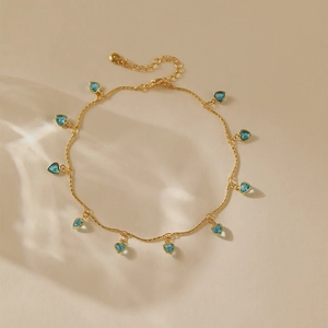 Gros plan d'une chaîne de cheville dorée avec plusieurs pendentifs bleus en forme de cœur