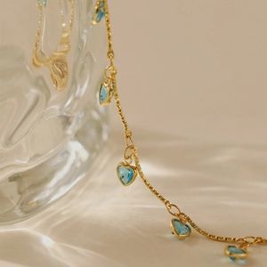 Détail d'une chaîne de cheville dorée avec des zircons bleus en cœur et finition brillante