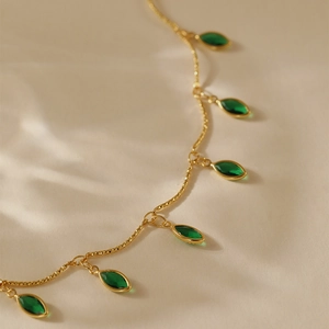 Close-up of golden twist chain anklet with marquise-cut green zircon stones