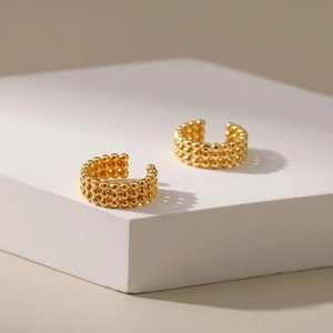 Vue macro d'un earcuff doré à trois rangées de perles sur un socle en pierre blanche