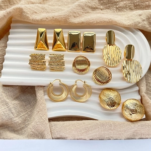 Set of six pairs of gold-plated geometric stud earrings and hoops on a white wavy board