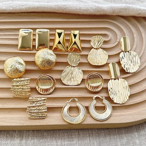 Collection of geometric 18K gold plated earrings displayed on a wooden tray