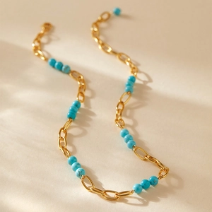 Gros plan d'un collier en chaîne dorée orné de perles turquoise sur fond beige