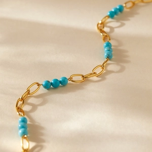 Vue détaillée des perles de turquoise vintage et chaîne dorée sur surface texturée
