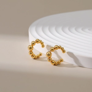 Détail du bijou d'oreille doré orné d'une séquence de perles métalliques polies