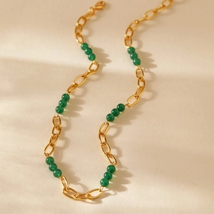 Détail de collier à maillons dorés et perles vertes sur un fond beige minimaliste