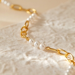 Détail macro d'un collier chaîne en or avec perles blanches lustrées et maillons polis