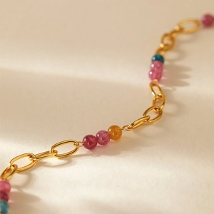 Détail d'une chaîne dorée bohème avec des perles colorées roses, jaunes et bleues