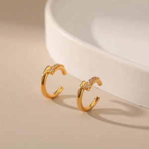 Gros plan d'un ear cuff doré en forme de C avec bordure sertie de strass brillants