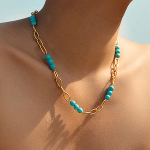 Collier bohème à chaîne dorée avec perles turquoises porté sur le cou d'un mannequin