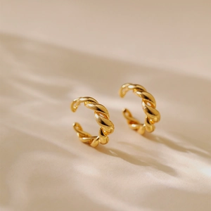 Élégantes boucles d'oreilles torsadées plaquées or 18 carats sur un tissu beige minimaliste