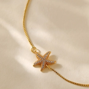 Close-up of gold plated box chain bracelet featuring a zircon-studded starfish pendant