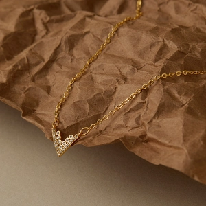 Dettaglio della collana con ciondolo a V dorato e zirconi su sfondo di carta ruvida