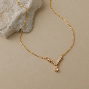 Dettaglio della collana dorata a V con zirconi scintillanti e pendente a goccia d'acqua