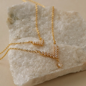 Dettaglio macro di collana a V dorata con zirconi baguette su una pietra bianca