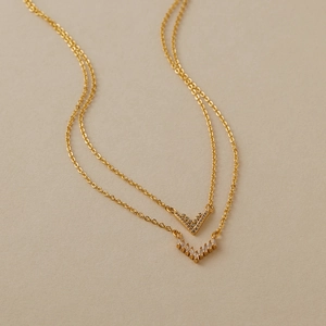 Dettaglio della collana doppia dorata con ciondoli a V e zirconi brillanti incastonati