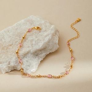 Detail of pink oval stone anklet with gold beads and lobster clasp on stone surface
