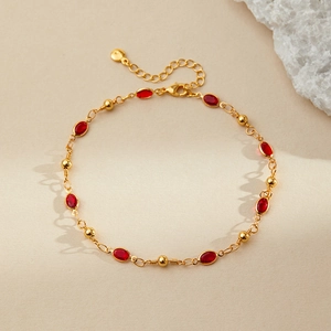 Detail of bohemian gold-plated anklet featuring red oval gemstones and lobster clasp closure