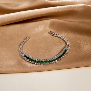 Macro detail of triple-layer silver bracelet with emerald green crystals on gold silk