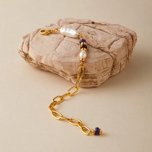 Dettaglio di un bracciale a catena dorata con perle barocche e ametista su una roccia