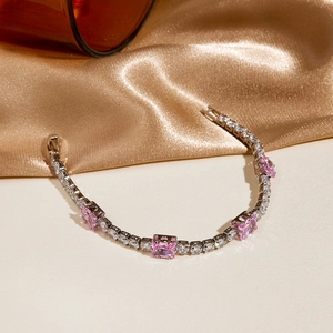 Macro shot of silver tennis bracelet with pink square zircons on golden silk fabric