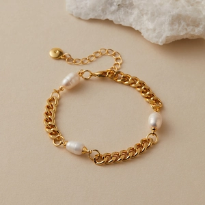 Dettaglio del bracciale bohémien con perle e catena cubana dorata con estensione su fondo beige