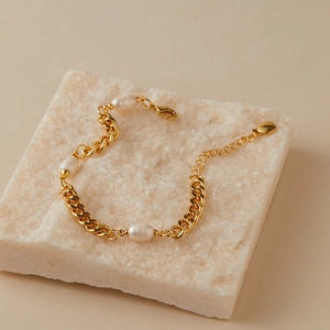 Dettaglio di elegante bracciale a catena dorata con perle d'acqua dolce e chiusura a moschettone