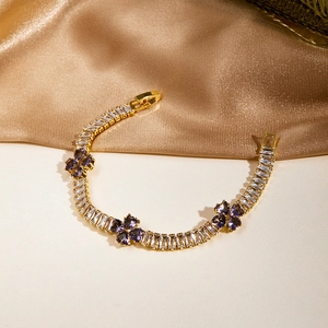 Detailed close-up of golden tennis bracelet with purple clover charms and white zircons