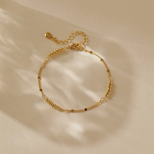 Detail eines 18K vergoldeten Armbands mit winzigen Perlen und polierten flachen Scheiben