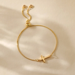 Detail of adjustable gold cross bracelet with box chain and heart charm ends