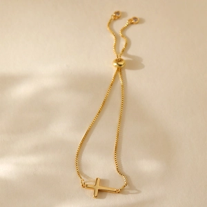 Detail of adjustable gold box chain bracelet with horizontal cross and slider bead