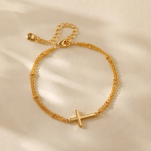 Detail of gold plated double-layer bracelet featuring cross pendant and adjustable chain