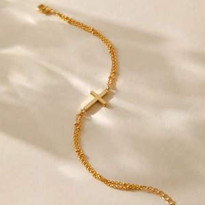 Detailed view of gold plated double chain bracelet with a polished cross charm