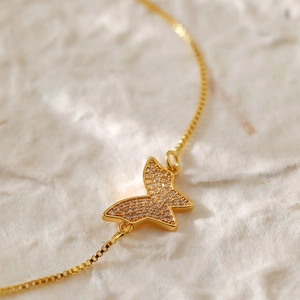 Close-up of a gold box chain bracelet featuring a sparkling crystal butterfly charm