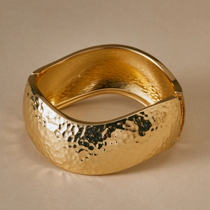 Macro shot of gold alloy wide cuff bracelet with hammered texture and irregular square shape