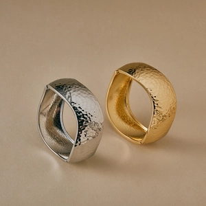 Detailed view of wide gold and silver cuffs with hammered texture and organic shape