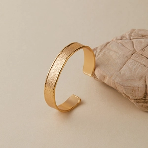 Detailansicht eines goldenen Manschettenarmbands mit Hammerschlag-Textur und glatter Innenseite