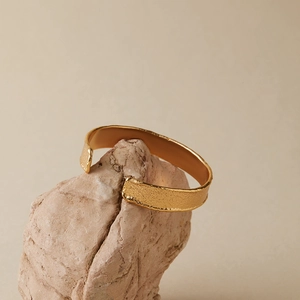 Detail der Lava-Textur und der mattgoldenen Oberfläche eines unregelmäßigen Manschettenarmbands