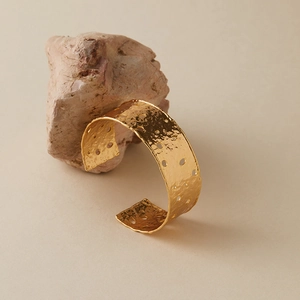 Detailaufnahme der goldenen gehämmerten Manschette mit geometrischem Lochmuster