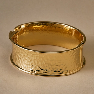 Detail of wide gold hammered cuff bracelet with side hinge closure and metallic texture