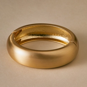 Detailed macro view of gold-tone wide hinge bangle with brushed matte finish and hammered texture