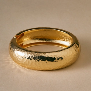 Detailed close-up of a wide golden hammered metal cuff bracelet with a hinge design