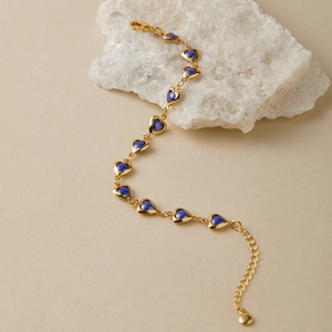 Detailed shot of gold bracelet with heart-shaped blue stones on a crystal stone base