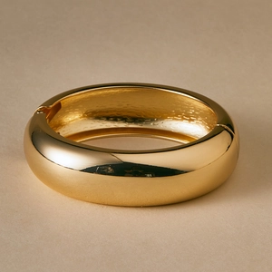 Detailed close-up of a polished gold-finished hinged metal bangle with a glossy surface
